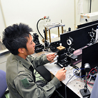 <span class="qrinews-figure-title">2012年10月26日 修士2年の大庭さん</span>　ラマン分光器を用いてトレハロース水溶液の分子構造を研究しています。（撮影場所：<a href="http://frontier.phys.kyushu-u.ac.jp/liquid-phys/" target="_blank">構造物性研究室</a>）