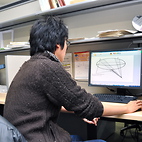 <span class="qrinews-figure-title">2013年1月17日 修士2年の田中さん</span>　非等方的で平均曲率が0の曲面について研究しています。（撮影場所：<a href="http://www.math.kyushu-u.ac.jp" target="_blank">数理学研究教育棟 院生室4</a>）