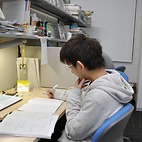 <span class="qrinews-figure-title">2016年2月8日 修士1年の清水さん</span>　表現論とゼータ関数を融合したウィッテンゼータ関数を研究しています。（撮影場所：<a href="http://www.math.kyushu-u.ac.jp" target="_blank">数理学府_院生室</a>）